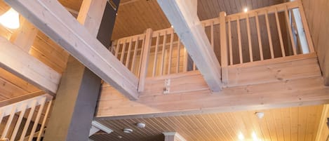 Una habitació ampla amb sostre alçat, bigues de fusta a la vista, un balcó i armaris encastrats.