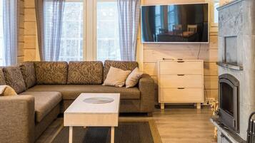 Un salon chaleureux avec un canapé, une table basse, un téléviseur, une cheminée et une fenêtre avec des rideaux.