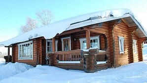 A wooden cabin with a porch and windows, surrounded by snow.