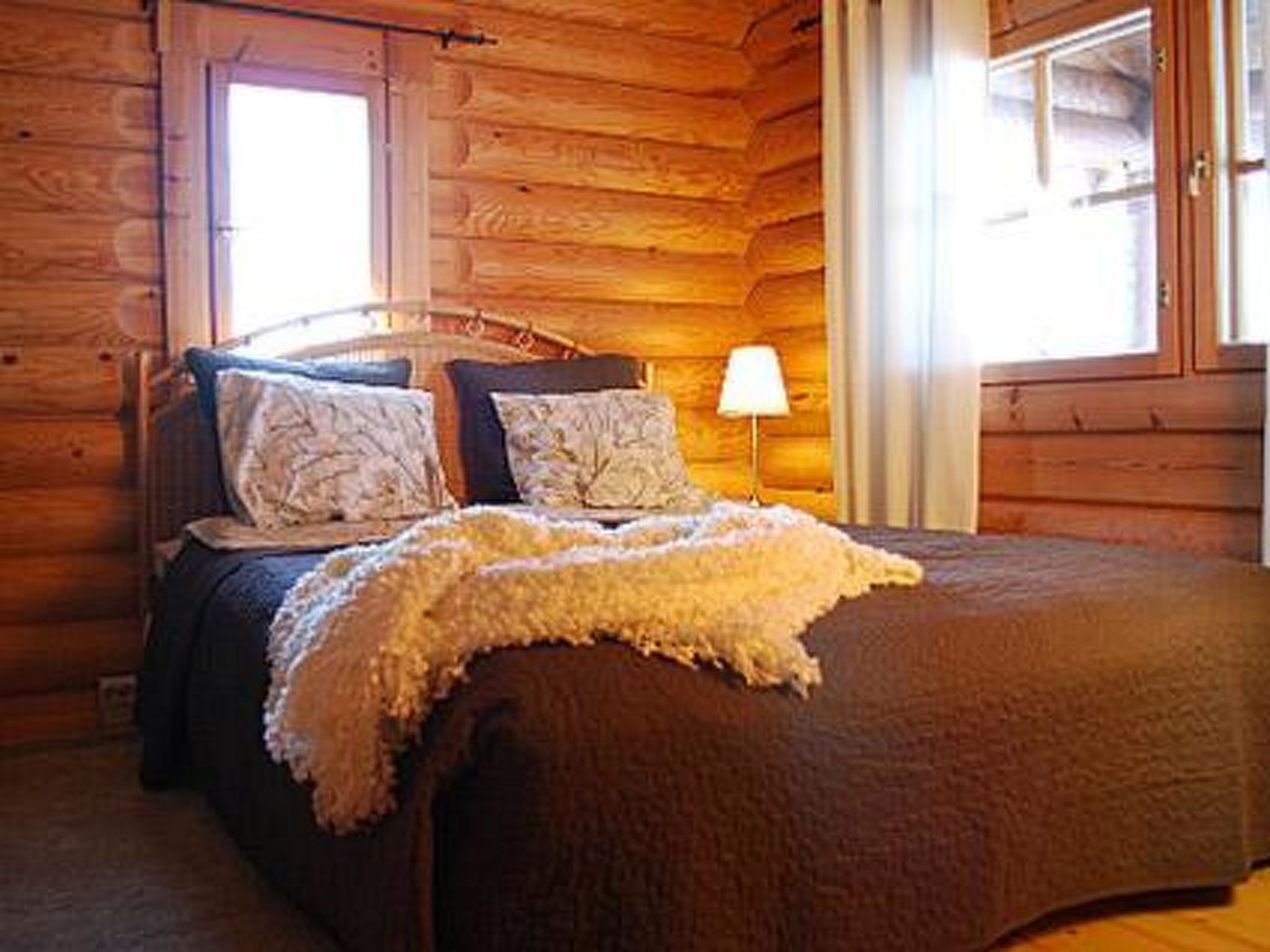 Habitació d'estil cabana de fusta amb un llit, almoines i una làmpada.
