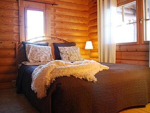 A wooden cabin-style room with a bed, pillows, and a lamp. - Villiruusu by Interhome (Sonkajärvi)