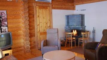 A cozy log cabin interior with a fireplace, wooden walls, a television, and comfortable seating.