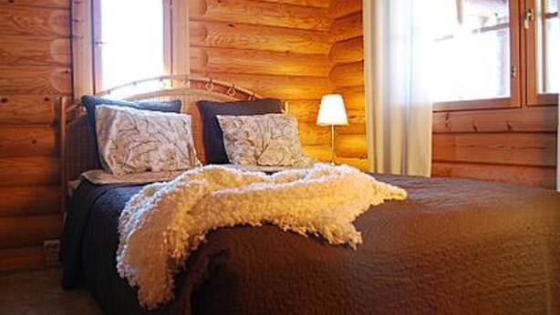A wooden cabin-style room with a bed, pillows, and a lamp.
