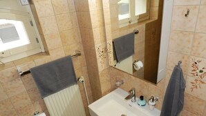 Een badkamer met beige tegels, een wit wastafelmeubel, een spiegel en een handdoekrek.