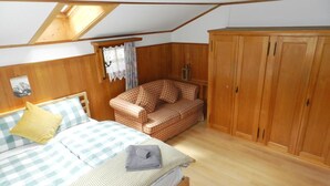 Een slaapkamer met een bed, een gestreept sofa, een kledingkast en een dakraam.