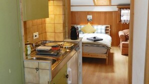 Een compacte keuken met een fornuis, spoelbak en een klein eethoekje, met een bed op de achtergrond.