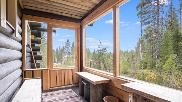 A log cabin interior with a wooden staircase, large windows, a wooden bench, and a rustic rug.