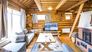 A cozy log cabin interior with a sofa, a TV, a fireplace, and wooden walls.