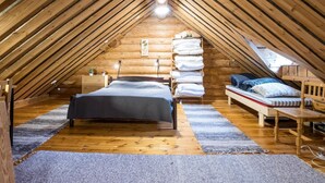 A cozy attic bedroom with a sloped wooden ceiling, a bed, a bench, and a shelf with folded blankets.