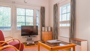 Una habitación con televisión, una mesita, una silla, un armario y una ventana con cortinas.