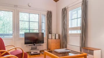 A room with a television, a small table, a chair, a cabinet, and a window with curtains.