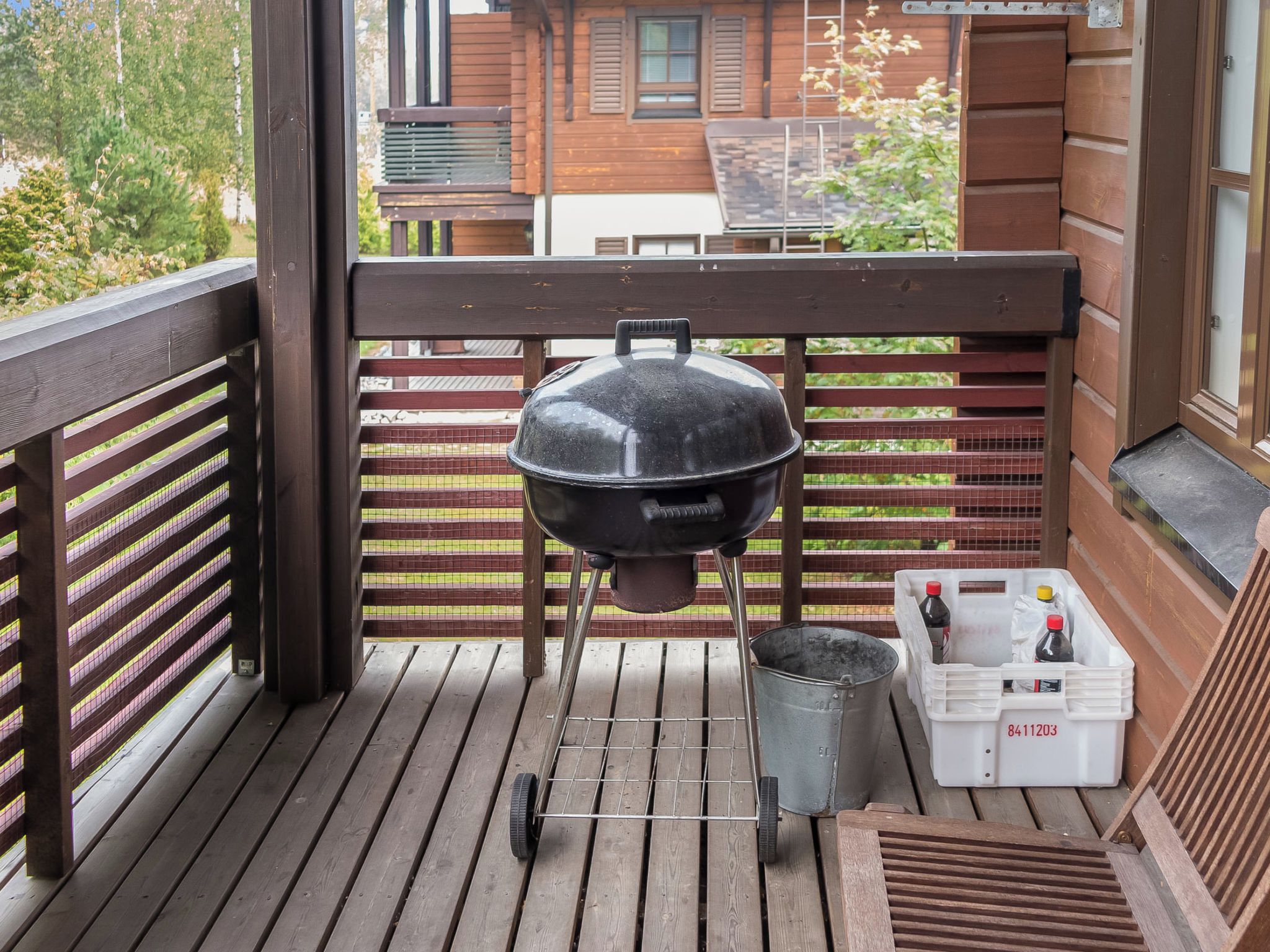 En grill på ett trädäck, tillsammans med en metallhink och en vit kylväska med ett rött lock.