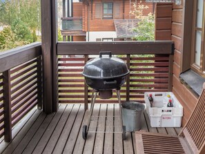 Una parrilla de barbacoa en una terraza de madera con un cubo de metal y un enfriador blanco con tapa roja.
