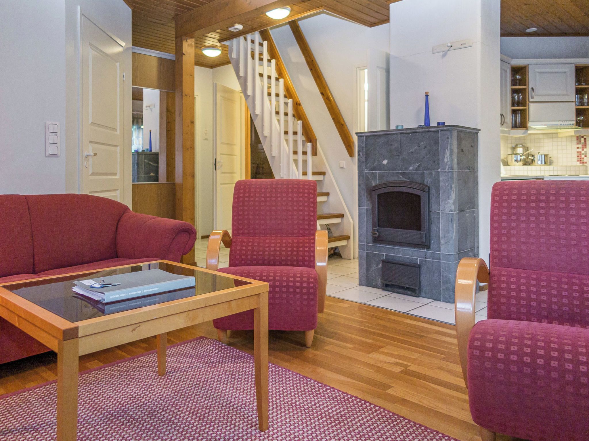 A living room with a red sofa, matching armchairs, a glass coffee table, and a fireplace.