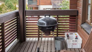 Una terraza de madera con una parrilla, un cubo de metal y un enfriador blanco con tapa roja.