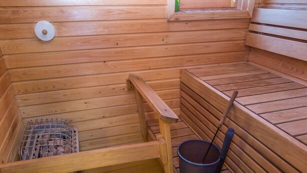 Una sauna de madera con bancos, un balde y un estante metálico.