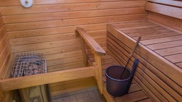 A wooden sauna with benches, a bucket, and a metal rack.