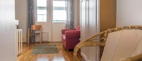 Une pièce avec un plafond en bois, un canapé rouge, un fauteuil en osier et un meuble blanc.