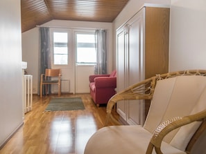 Una habitación con techo de madera, un sofá rojo, una silla de mimbre y un armario blanco.