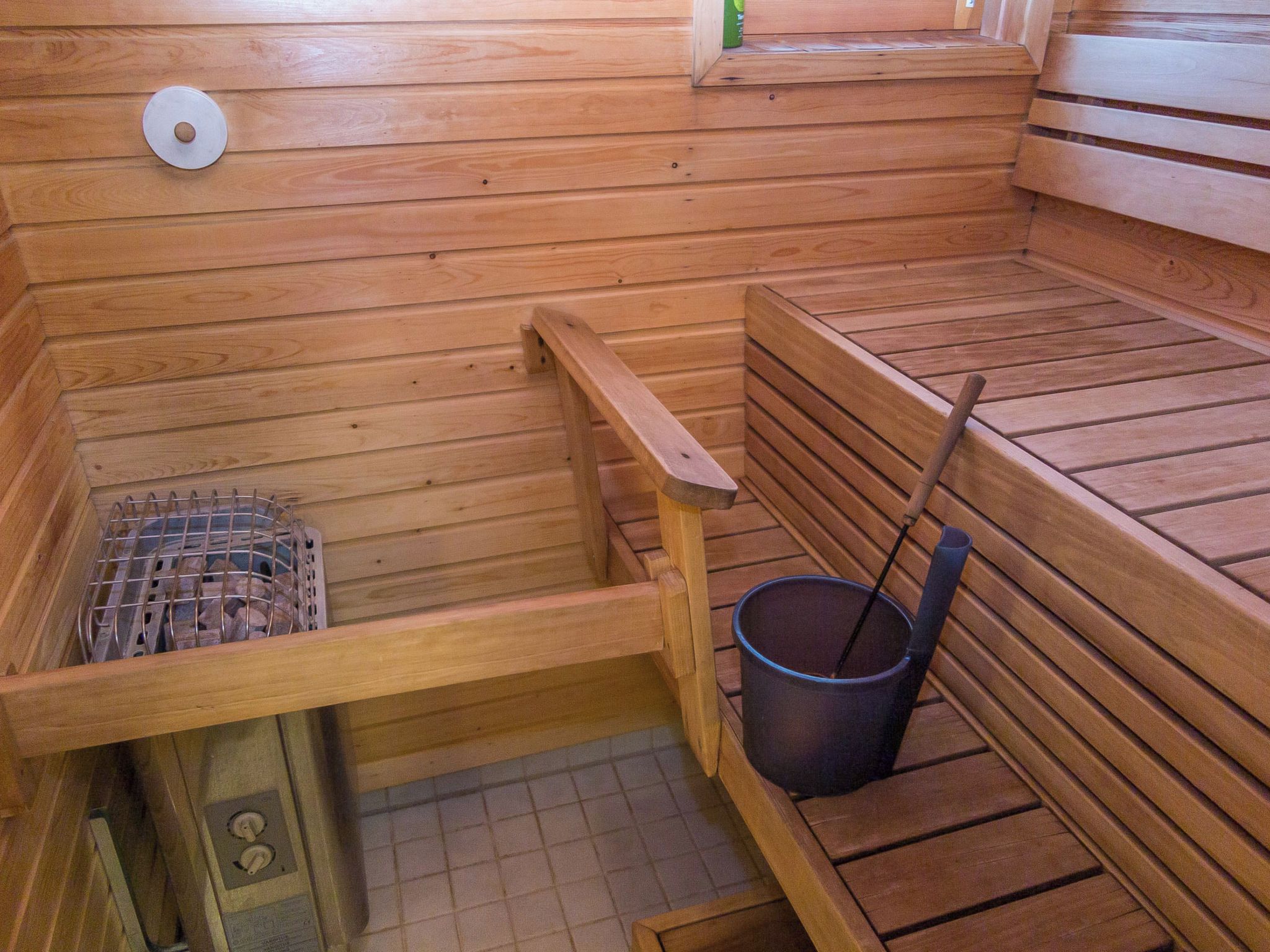 Una sauna con bancos de madera, una rejilla metálica y un cubo con mango largo.