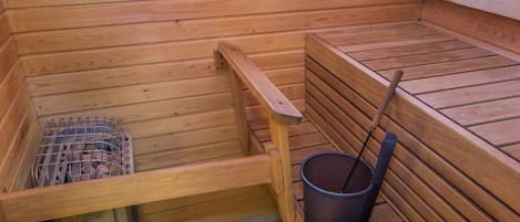 A sauna with wooden benches, a metal grate, and a bucket with a long handle.