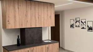 A modern kitchen with wooden cabinetry, a black countertop, and a decorative ceiling beam. - Ferienhaus Adonis by Interhome (Saas-Grund)