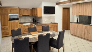 A modern kitchen with wooden cabinets, a built-in oven, and a dining area with a marble table and chairs. - Ferienhaus Adonis by Interhome (Saas-Grund)