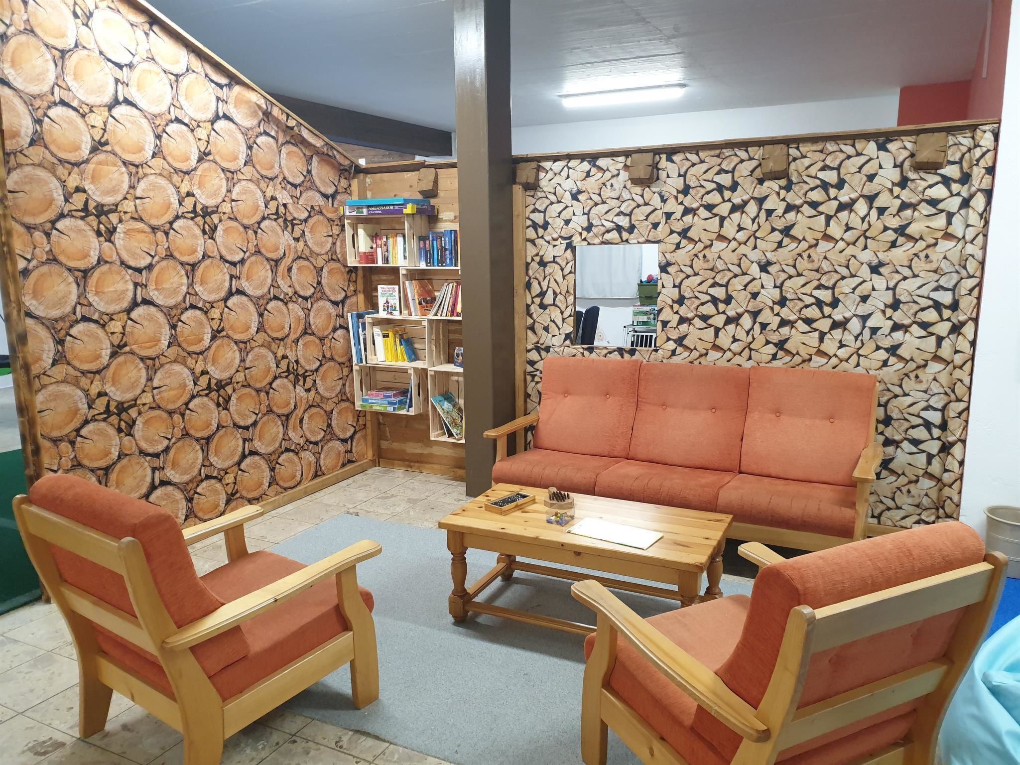 A cozy room with a sofa, two armchairs, a coffee table, and a bookshelf against a wall with a wood log pattern.
