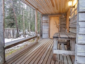 Uma cabana de madeira com um banco e uma mesa, uma porta de madeira e vista para uma floresta nevada.