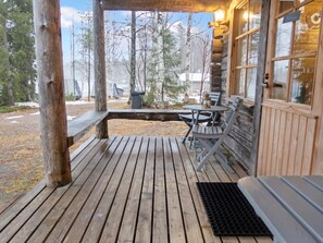 Eine Holzterrasse mit Tisch, Stühlen und einer Bank, sowie ein Fenster mit Blick auf Bäume.