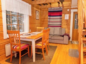A cozy cabin interior with a wooden dining table, chairs, a sofa, and a window with curtains.