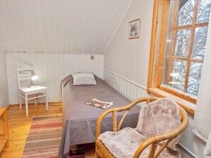 A small, cozy room with a single bed, a chair, a desk, and a window with a view of trees.