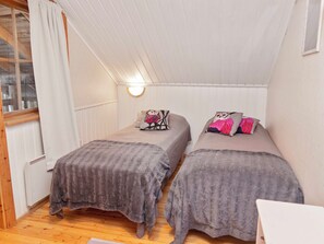 Quarto pequeno e aconchegante com duas camas de solteiro, janela com cortinas e luminária fixada na parede.