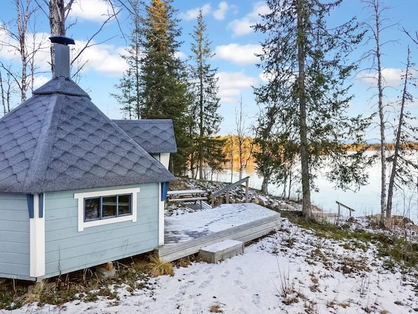 Pieni mökki, jossa on jyrkkästi kallistuva katto, savupiippu ja terassi, joka johtaa laituriin.