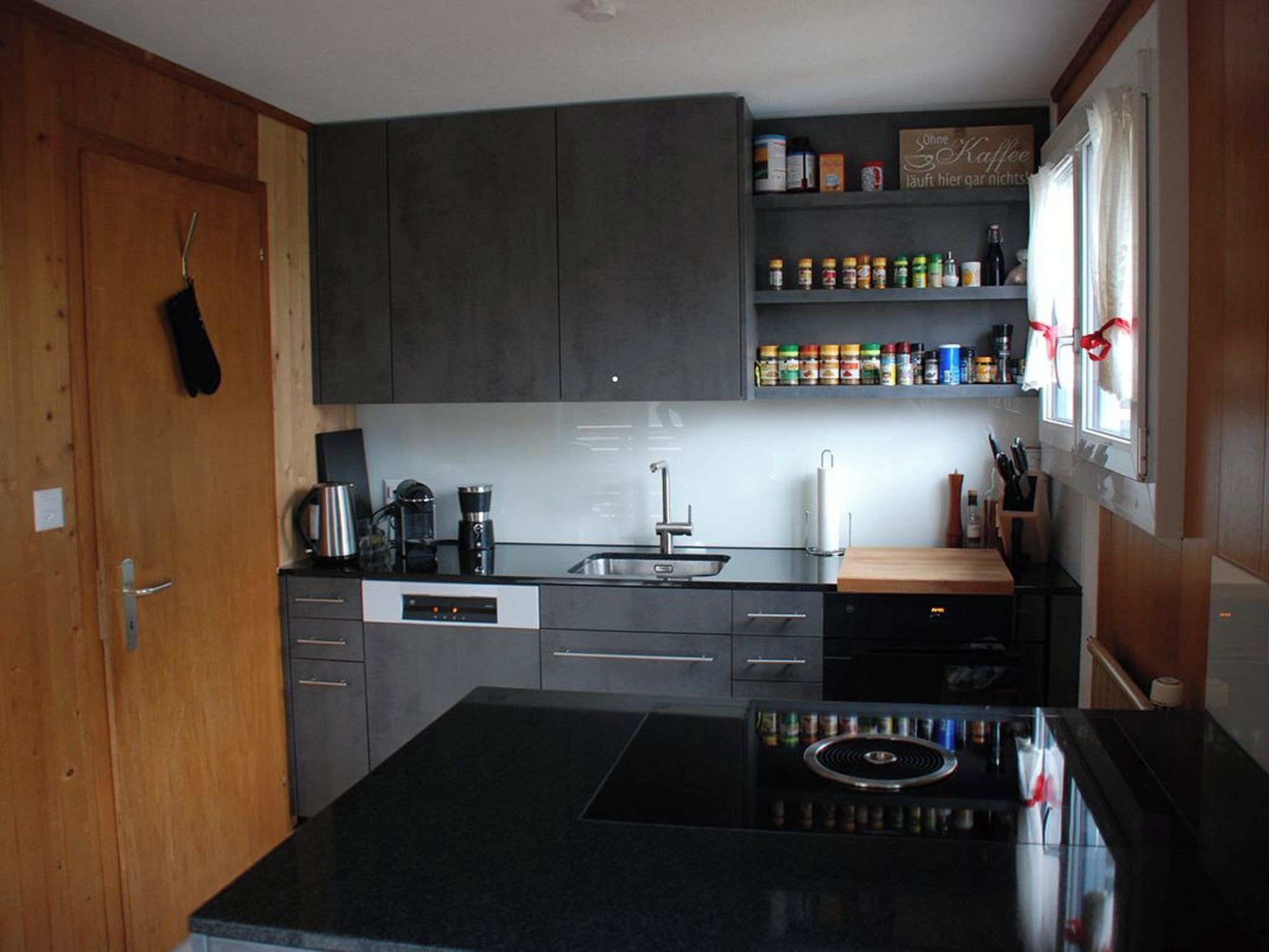 A modern kitchen with a black countertop, stainless steel appliances, and a variety of spices on shelves.