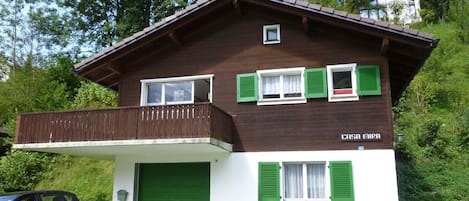 A two-story house with a balcony, green shutters, and a green garage door.