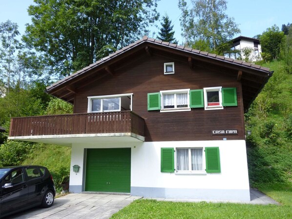 A two-story house with a balcony, green shutters, and a green garage door.