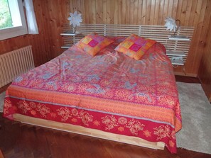 A bed with a patterned bedspread and two pillows, a wooden headboard, and a window with curtains.