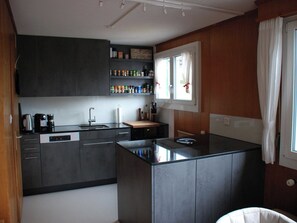 A modern kitchen with dark cabinetry, a built-in dishwasher, and a window with curtains.