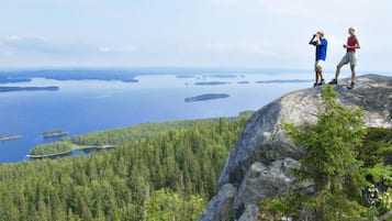 Kaksi ihmistä seisoo kallioisella kohdalla, josta avautuu näkymä metsäiselle alueelle ja vesistölle.