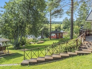 Una terraza de madera que lleva a una cabaña pequeña con vista al río, rodeada de abundante vegetación.