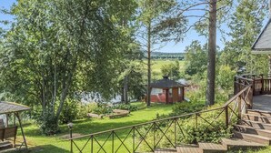 Une terrasse en bois mène à un chalet doté d’un petit porche, le tout étant entouré d’une végétation luxuriante et bordé par un lac.