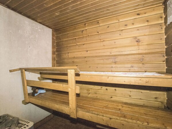 A wooden bunk bed with a ladder, a small shelf, and a pair of slippers.