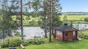 Une cabane en rondins au bord d’un lac, avec une zone herbeuse, un banc et un petit jardin.