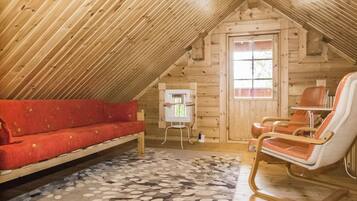 Una habitación cálida en el ático con techo inclinado de madera, un sofá rojo, un sillón mecedor y una alfombra estampada.