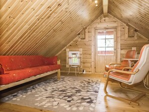 A cozy attic room with a wooden sloped ceiling, a red sofa, a rocking chair, and a patterned rug.
