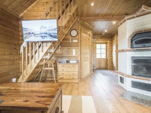A wooden cabin interior with a television, a fireplace, a kitchen area, and a staircase. - Liisakallela by Interhome (Sonkajärvi)