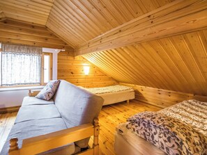 Een gezellig slaapkamer op zolder met een schuine houten balkenplafond, een bank, een enkel bed en een nachtkastje.