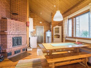 Un intérieur de chalet chaleureux avec une cheminée en briques, une table à manger en bois et de grandes fenêtres.