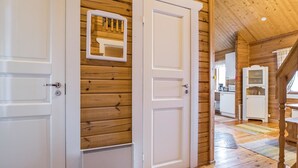 Interior de madera con una puerta blanca, un espejo y una cocina visible a través de una puerta abierta.